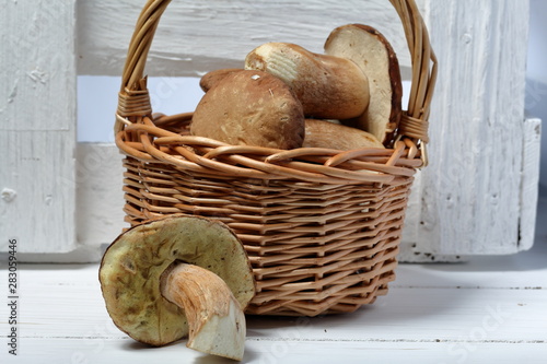 Wicker basket with porcini mushrooms. Nearby lies one mushroom. Near a box of boards.