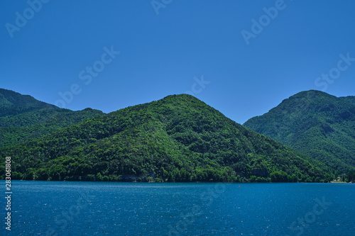 Panoramic view of Lake Ledro in the north of Italy In the Alps. Blue lake, in the background green mountains, blue sky.
