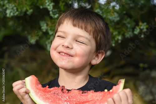 Happy boy eating healthy watermelon in garden. Child with a big slice of watermelon