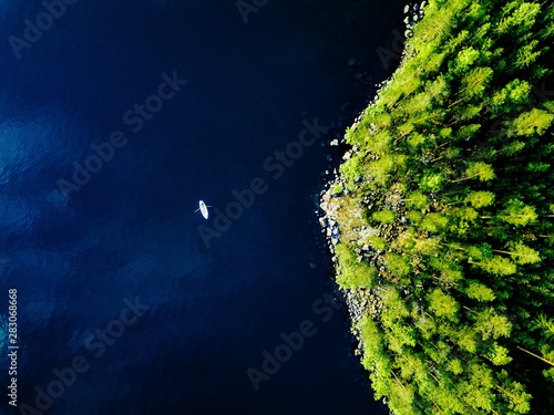Aerial view of blue lake with a fishing boat and green forests with rocks in Finland.