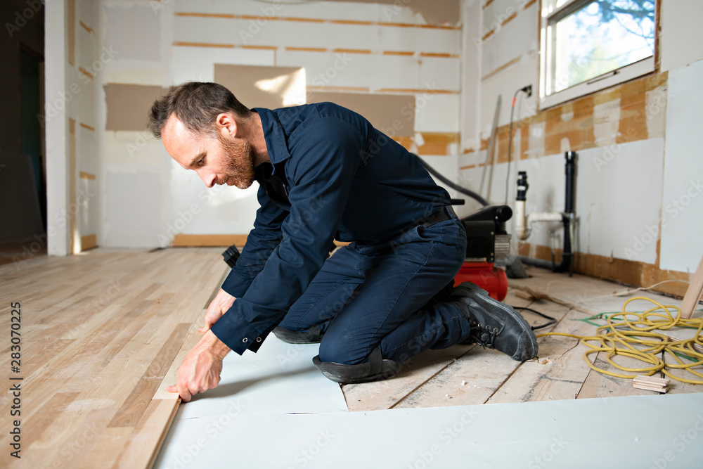 A Male Worker install wood floor on a house - obrazy, fototapety, plakaty 