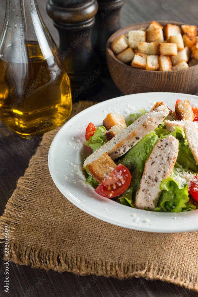 Fresh salad with delicious chicken breast, ruccola, spinach, cabbage, arugula and tomato on wooden background. Oil, salt and pepper.