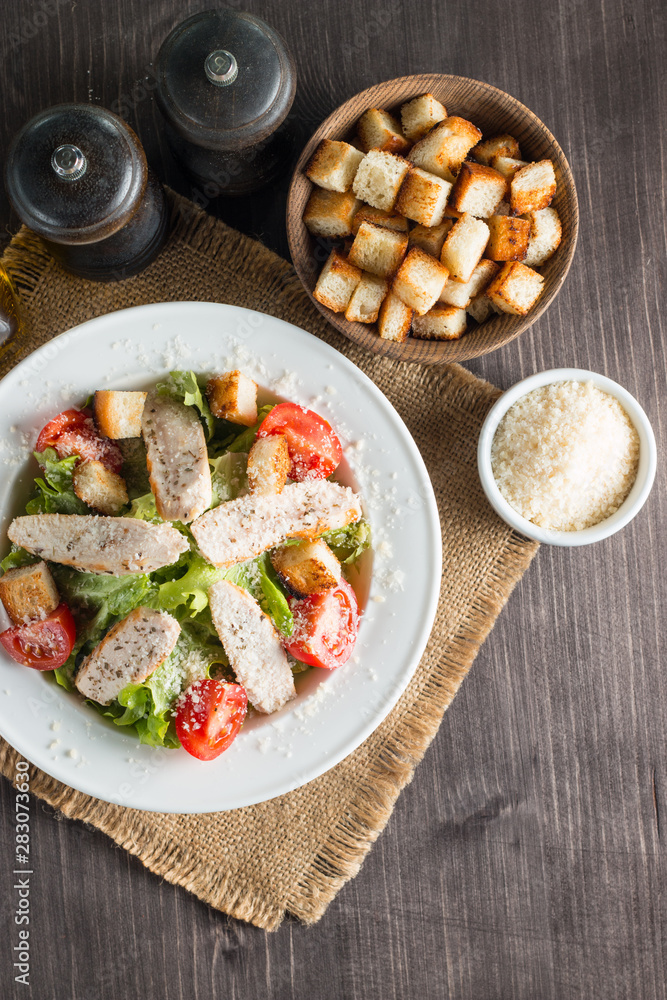 Fresh salad with delicious chicken breast, ruccola, spinach, cabbage, arugula and tomato on wooden background. Oil, salt and pepper.