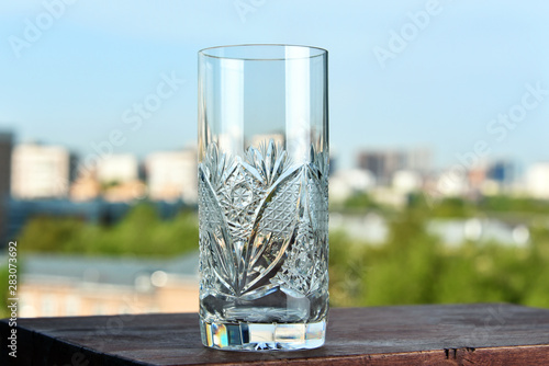 Empty crystal glass on a wooden desk on the background of a blurry cityscape