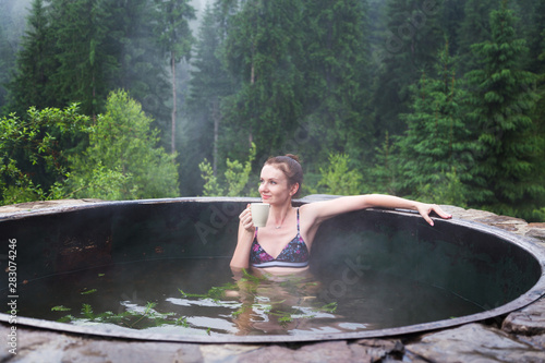 Girl relaxing in a hot vat on a background of mountain forests.
