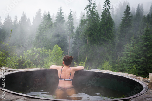 Girl relaxing in a hot vat on a background of mountain forests.