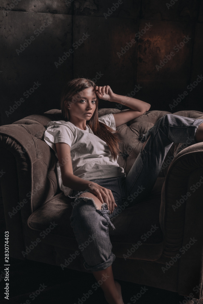 Sexy hot woman in shirt and jeans posing in loft studio on armchair on black background. Seductive glamour young girl model portrait. Sexy hot woman in shirt and jeans posing in loft studio on armchair on black background. Seductive glamour young girl model portrait.
