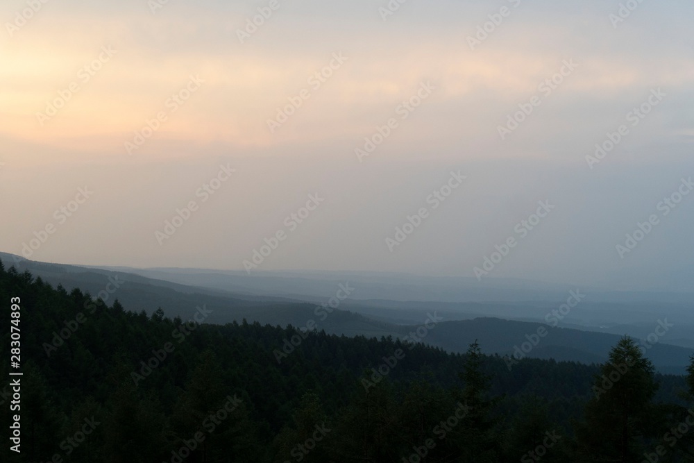 山に霧が掛かり森がシルエットになった夕焼けの風景／Nagano, Japan