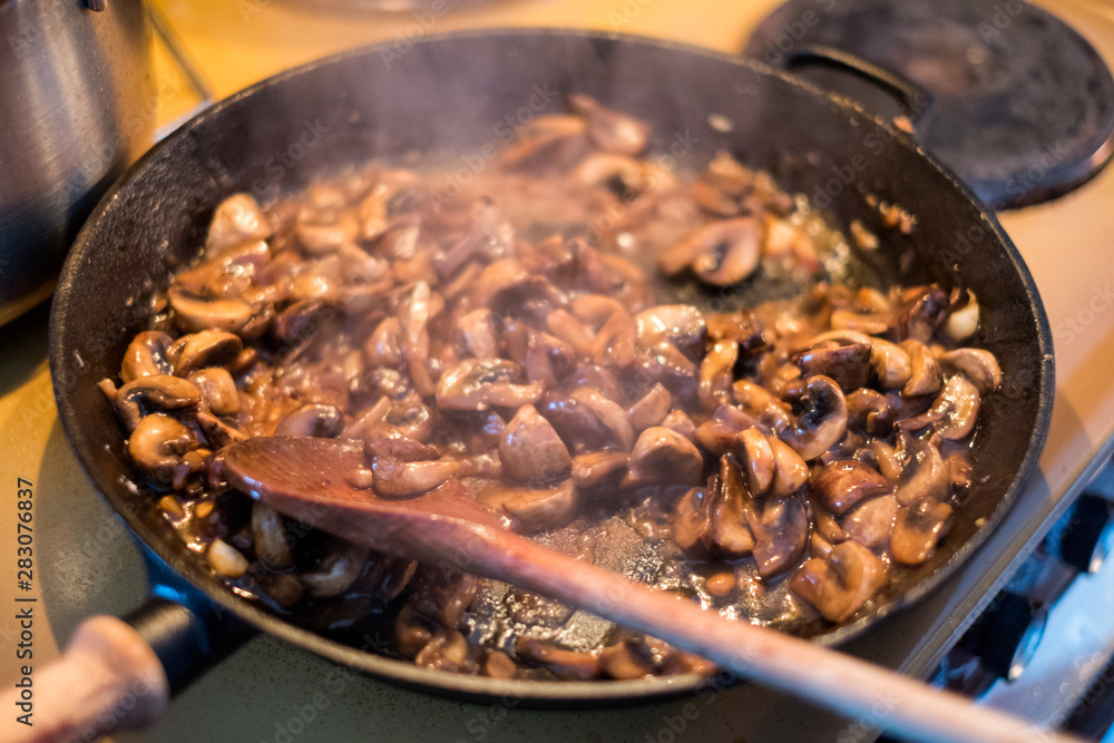 Fototapeta premium Cooking Champignons mushroom with wooden flipper a stir in pan