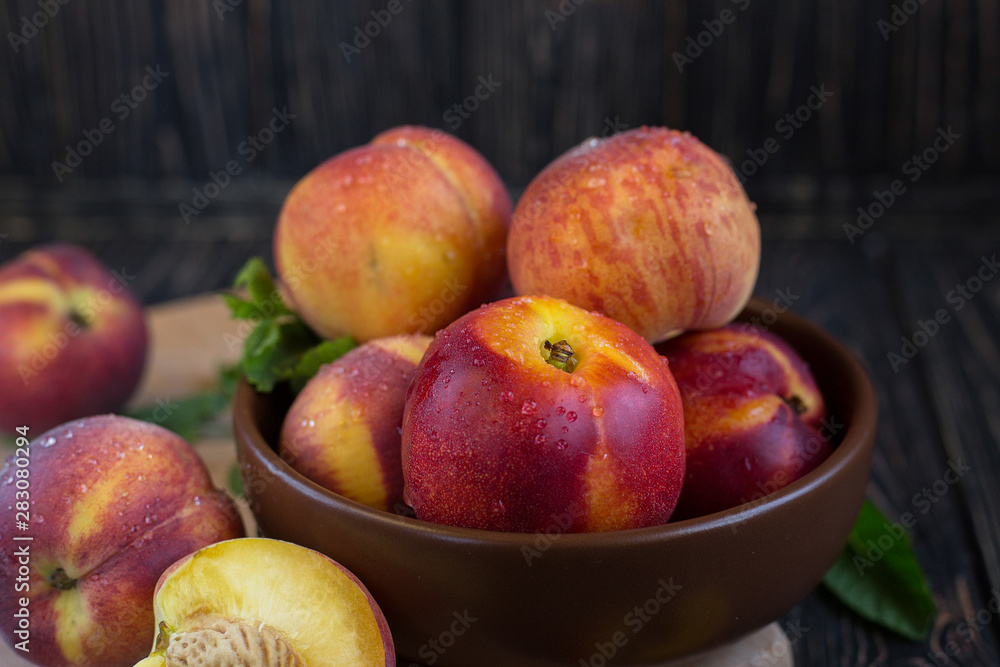 Delicious juicy orange-red peaches and nectarines on a dark background in a clay bowl. Dark background, still life of ripe summer fruits on a brown wooden table. Close-up Delicious juicy orange-red peaches and nectarines on a dark background in a clay bowl. Dark background, still life of ripe summer fruits on a brown wooden table. Close-up
