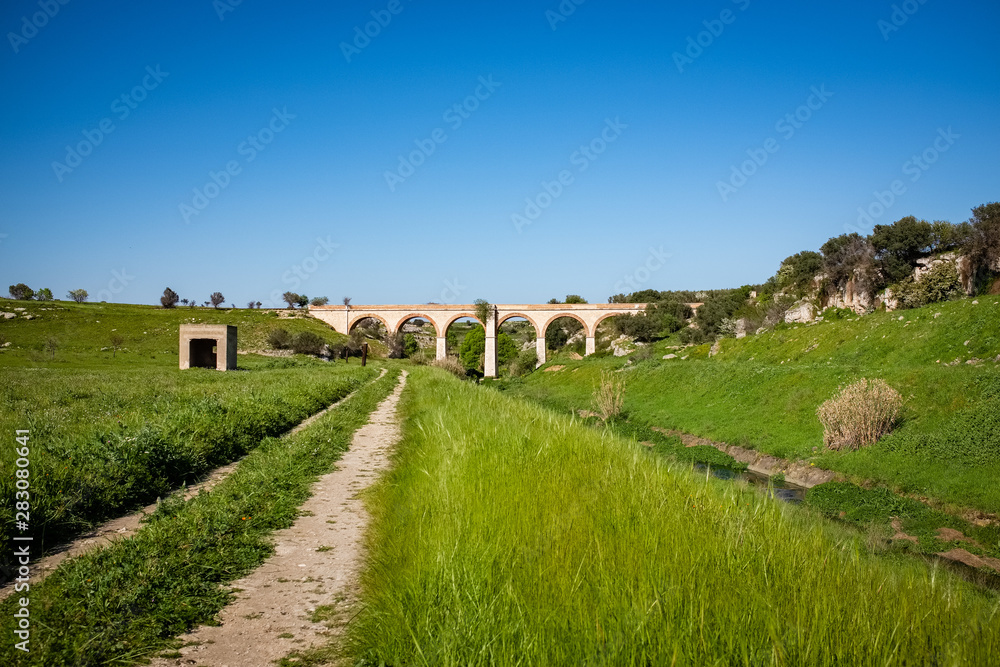 Beautiful old stone bridge of abandoned railway crossing a small river. Puglia region, Italy