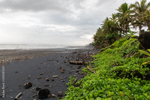 Black sand beach with green vegetation in a stormy day in Bali, Indonesia
