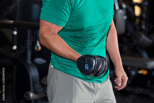 Torso of a young man in gym doing dumbbells
