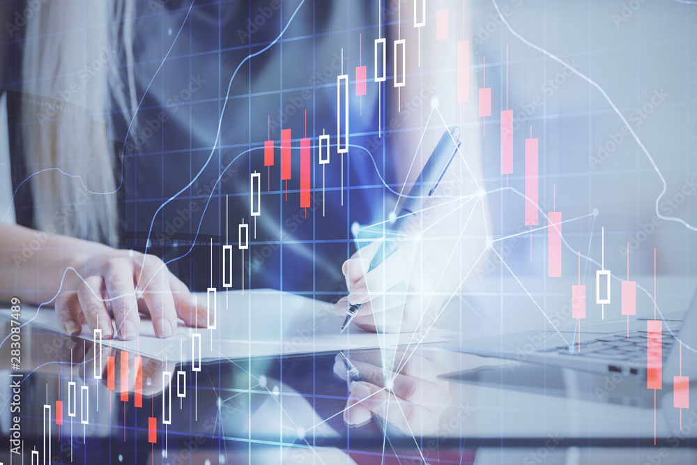 A woman hands writing information about stock market in notepad. Forex chart holograms in front. Concept of research. A woman hands writing information about stock market in notepad. Forex chart holograms in front. Concept of research.