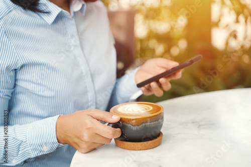 Close up of businesswoman using smartphone and drinking hot latte coffee in the morning at the cafe, business and lifestyle concept