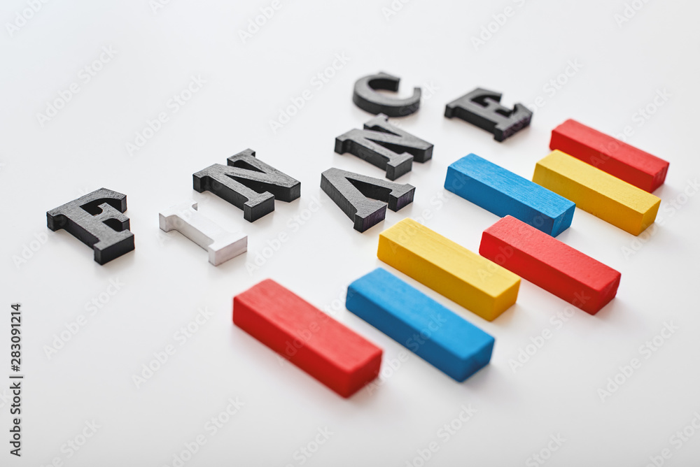 Finance word created with cubes alphabet letters near multi-colored wooden blocks lying diagonally Finance word created with cubes alphabet letters near multi-colored wooden blocks lying diagonally