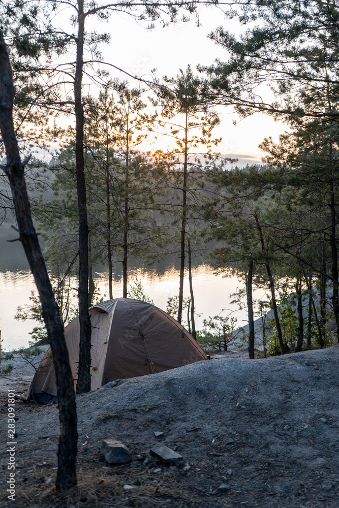 Tent in the woods on the shore of a quarry with blue water at dusk in