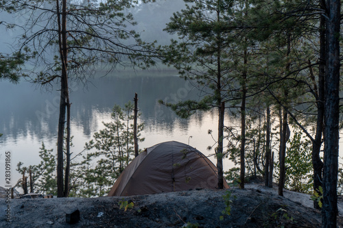 Tent in the woods on the shore of a quarry with blue water at dusk in summer Travel as a lifestyle and rest from the hustle and bustle
