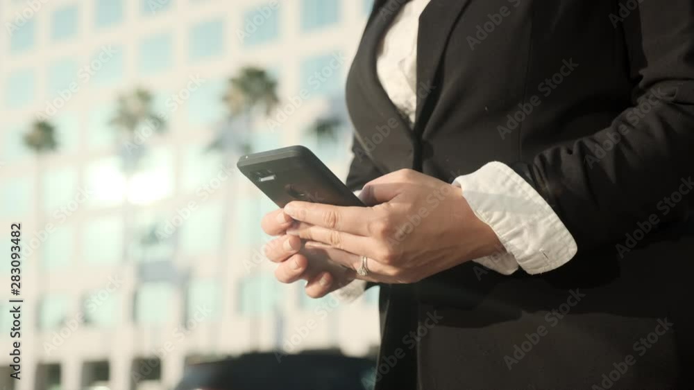 Business Woman Texting and Checking Phone in Front of Busy Corporate Office at Intersection Business Woman Texting and Checking Phone in Front of Busy Corporate Office at Intersection