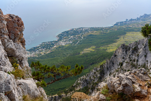 view of the resort city of Yalta from the top of Mount Ai-Petri, on a bright sunny day with clouds in the sky.