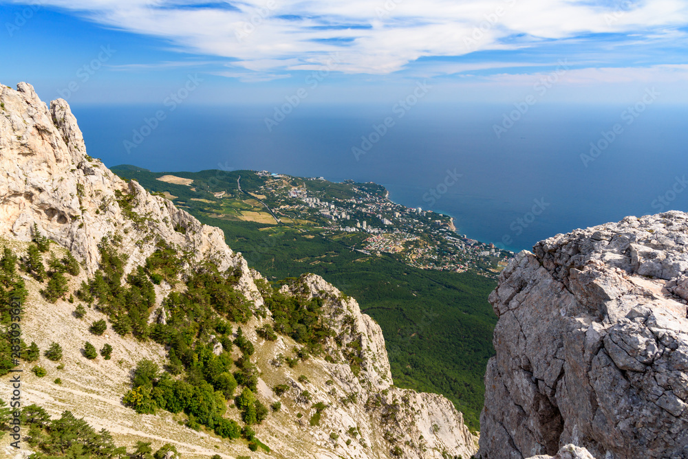 view of the resort city of Yalta from the top of Mount Ai-Petri, on a bright sunny day with clouds in the sky.