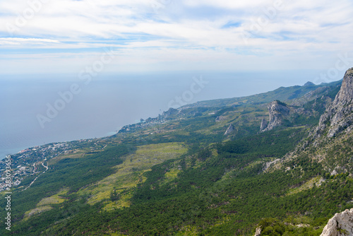 view of the resort city of Yalta from the top of Mount Ai-Petri, on a bright sunny day with clouds in the sky. © StockAleksey