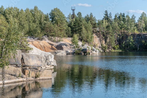 Scenic view of the blue water of the lake and the opposite rocky shore with growing trees against the blue sky on a summer sunny day. Traveling as a lifestyle