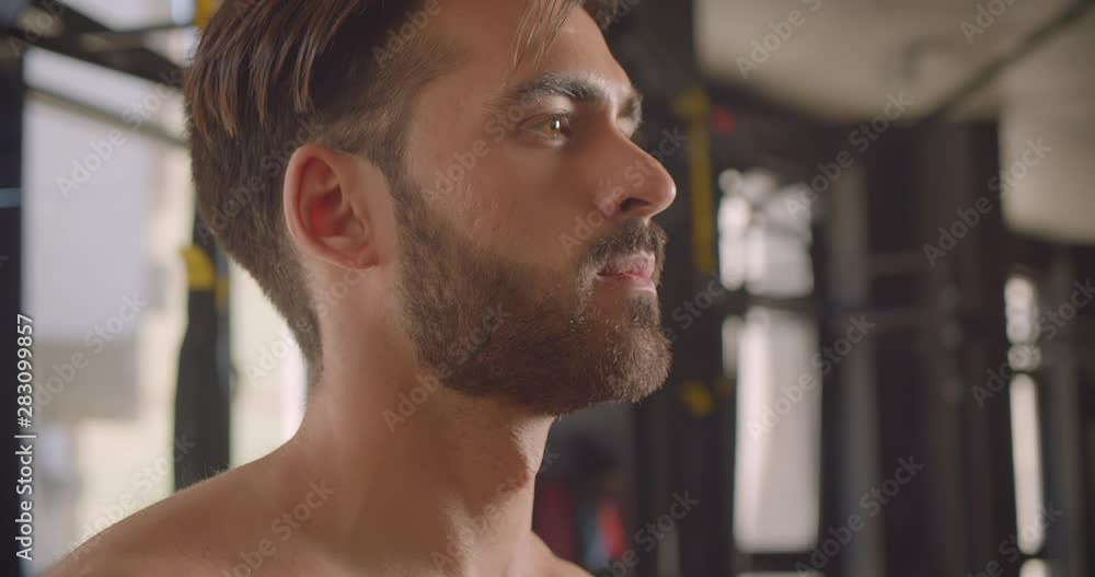 Closeup portrait of shirtless muscular caucasian man working out with dumbbells with effort standing in the gym indoors Closeup portrait of shirtless muscular caucasian man working out with dumbbells with effort standing in the gym indoors