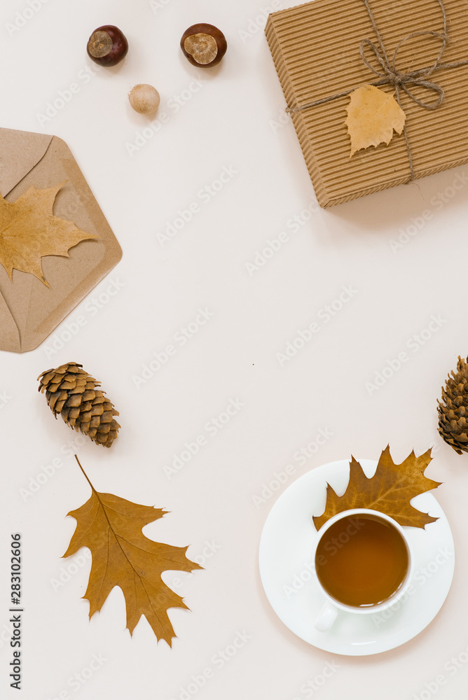 Autumnal flat lay with white knitted plaid, hot Cup of tea and fallen brown leaves, crab envelope, gift box. Top still life autumn concept on beige light background with copy space. Autumnal flat lay with white knitted plaid, hot Cup of tea and fallen brown leaves, crab envelope, gift box. Top still life autumn concept on beige light background with copy space.