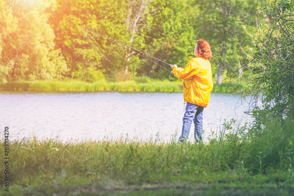 Woman in yellow jacket fishing spinning on the lake in sunlight Woman in yellow jacket fishing spinning on the lake in sunlight