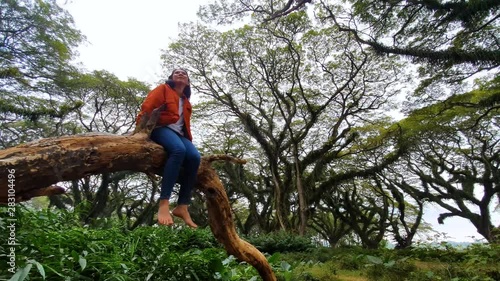 Young woman sitting on the tree branch while enjoying holiday in De Djawatan forest, Banyuwangi, East Java, Indonesia. Shot in 4k resolution photo