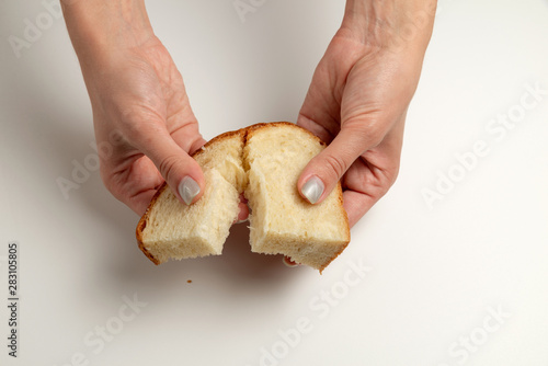 Female hands are giving the two pieces of the white bread on the white background/table. International Day to Assist the Poor