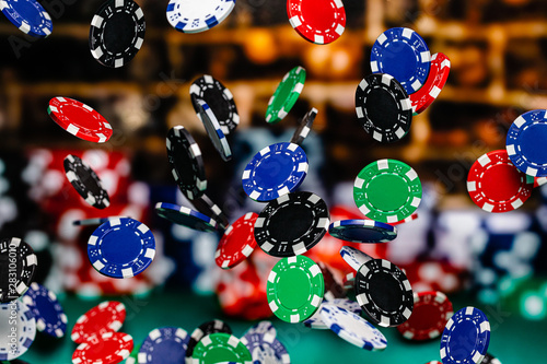 Red, Blue, Black and Green Clay Poker Chips cascading in front of a background of stacked poker chips.
