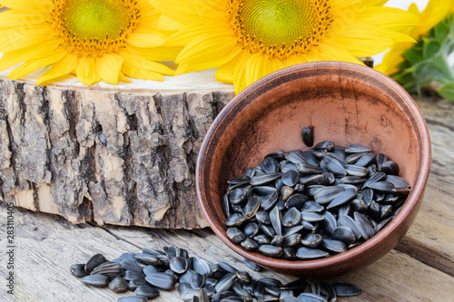 Yellow sunflowers and sunflower seeds in a bowl on a wooden background.