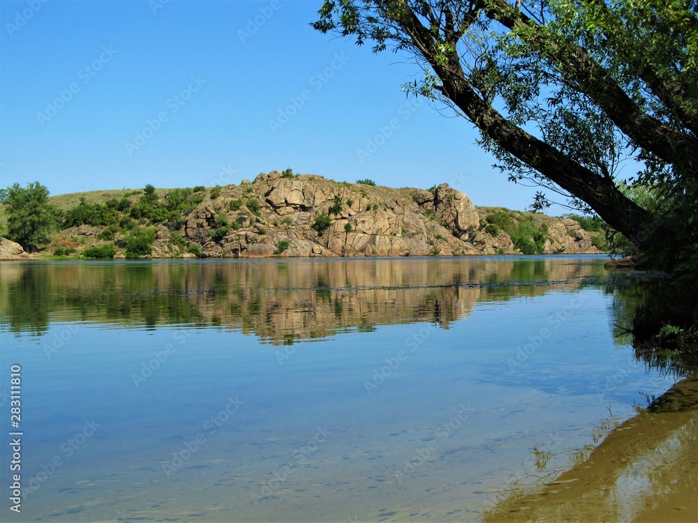 river landscape in summer, a tree over calm water with reflection of rocks