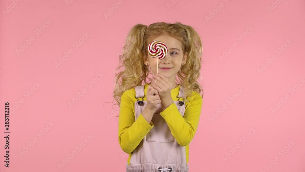 Little blond female is palying with a lollipop and smiling. Little blond female is palying with a lollipop and smiling.