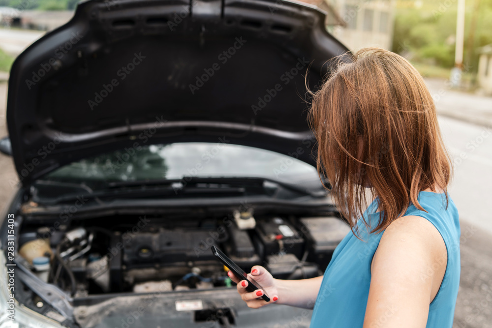 Young woman tourist driver standing by the road by the car with the hood open dead engine broken automobile malfunction repair in a summer day making a mobile phone call for help Young woman tourist driver standing by the road by the car with the hood open dead engine broken automobile malfunction repair in a summer day making a mobile phone call for help