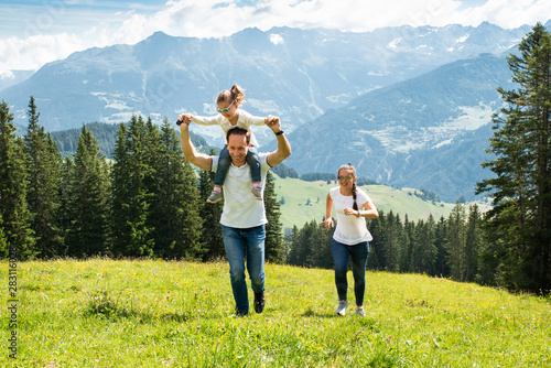 Family With Daughter Running On Field In Mountains