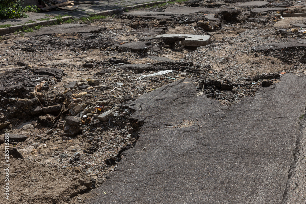 Large cracks, chips. Broken asphalt shifted landslide after flood. Destroyed road by water. Groundwater flushing. Concept of destruction of roads from nature. Consequences of flood. Broken street Large cracks, chips. Broken asphalt shifted landslide after flood. Destroyed road by water. Groundwater flushing. Concept of destruction of roads from nature. Consequences of flood. Broken street