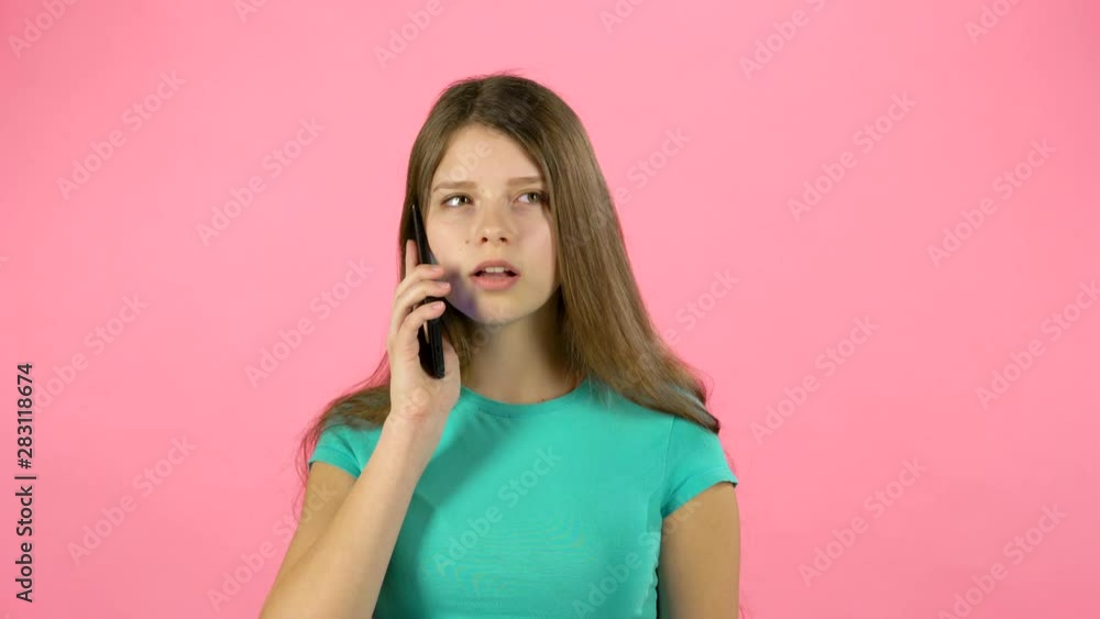 Girl talking using cell phone in studio against pink background. Girl talking using cell phone in studio against pink background.