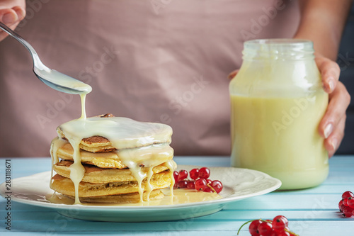 A girl in a pink apron adds condensed milk to pancakes. Delicious healthy food. Delicious pancakes with sauce and red currants. Close-up photograph of fresh natural dessert. photo