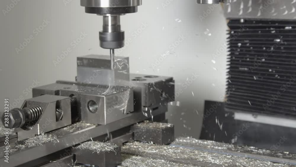 SLOW MOTION, CLOSE UP: Small drill cutting and shaving a piece of metal into an unfinished product. Shiny shavings fly off a block of aluminium being processed by a CNC drill. Micro machining process. SLOW MOTION, CLOSE UP: Small drill cutting and shaving a piece of metal into an unfinished product. Shiny shavings fly off a block of aluminium being processed by a CNC drill. Micro machining process.