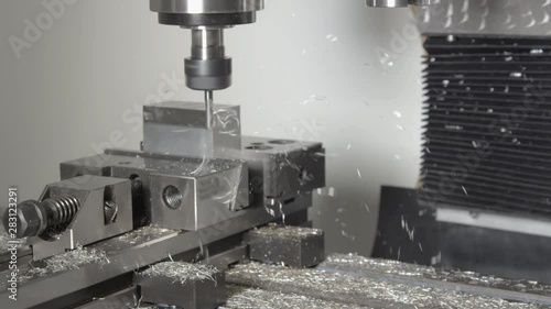 SLOW MOTION, CLOSE UP: Small drill cutting and shaving a piece of metal into an unfinished product. Shiny shavings fly off a block of aluminium being processed by a CNC drill. Micro machining process. photo