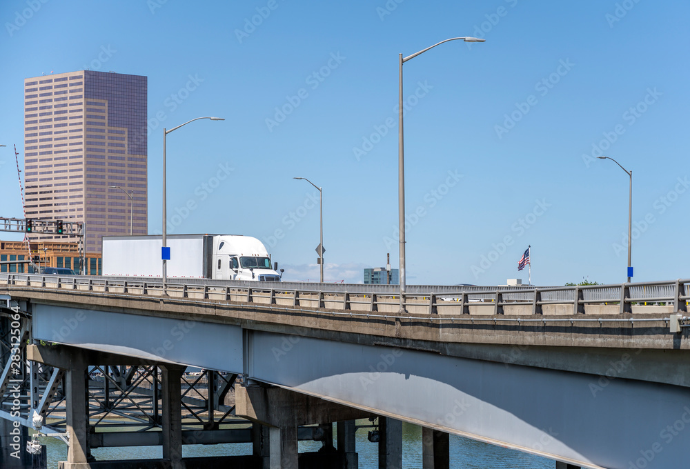 Big rig semi truck transporting cargo in semi trailer running on the bridge across Willamette River Big rig semi truck transporting cargo in semi trailer running on the bridge across Willamette River