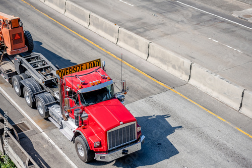 Big rig red semi truck with oversize load sign on the roof transporting oversized equipment on the semi trailer