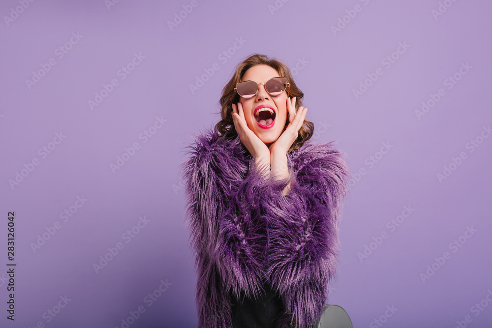 Excited girl laughing while posing in studio with purple interior. Indoor photo of sensual singing woman in fluffy fur coat enjoying photoshoot. Excited girl laughing while posing in studio with purple interior. Indoor photo of sensual singing woman in fluffy fur coat enjoying photoshoot.
