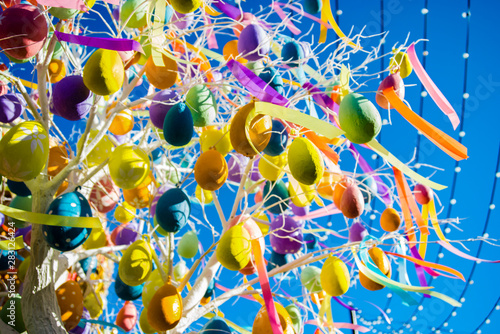 multicolored balloons and ribbons on the tree on blue sky with stripes background. Very colorful, part of celebration. Against bright sun and summer sky