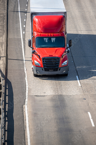 Bright red big rig semi truck transporting commercial cargo in dry van semi trailer driving on the road