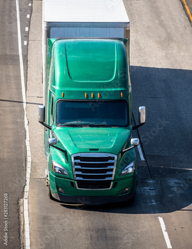Green big rig semi truck with semi trailer transporting cargo running on multyline highway