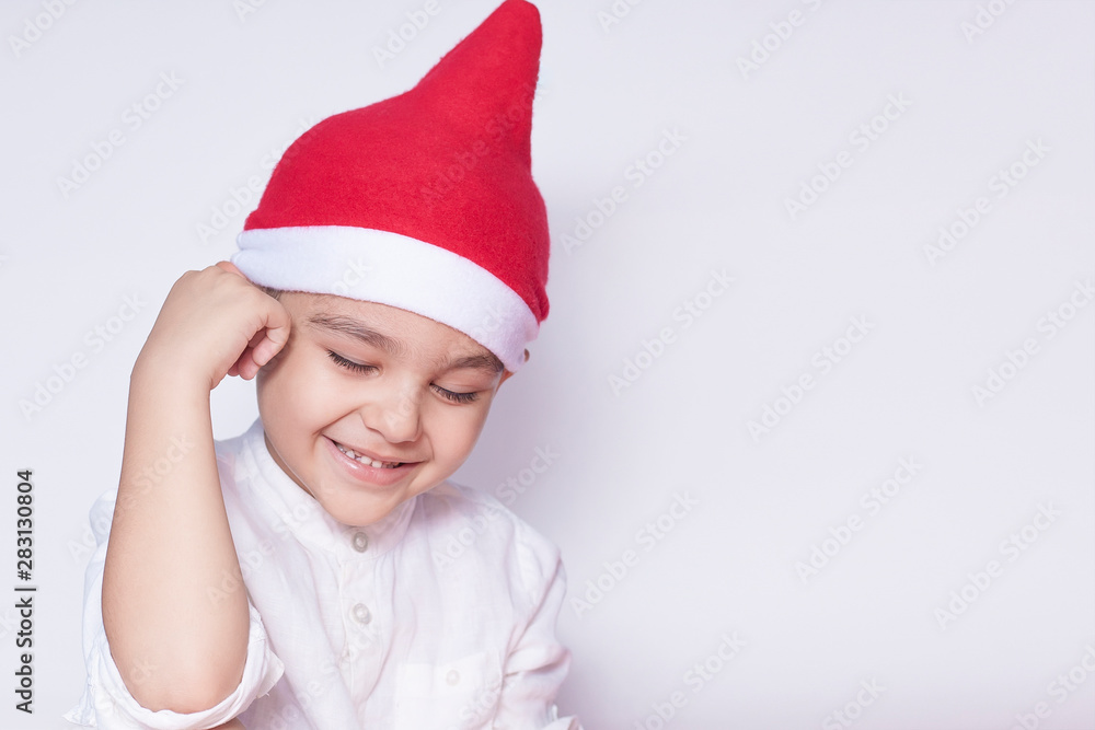 Portrait of smiling shy boy. Six-year-old kid shy and smiling. Celebrating Christmas. 6-7 year old child with Santa hat. Portrait of smiling shy boy. Six-year-old kid shy and smiling. Celebrating Christmas. 6-7 year old child with Santa hat.